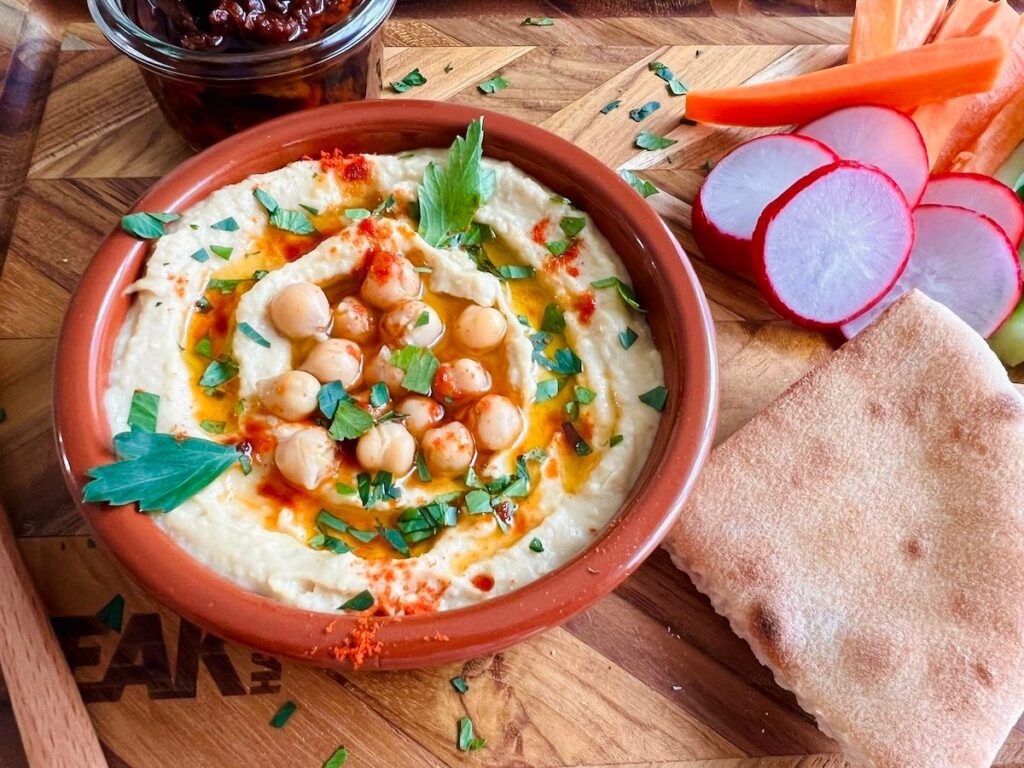 Shio-koji Yoghurt Salad Open Sandwich Shio-koji hummus, served in a terracotta dish with cucumbers, carrots, warm pita bread and sun-dried tomatoes. Garnished with chickpeas, paprika an